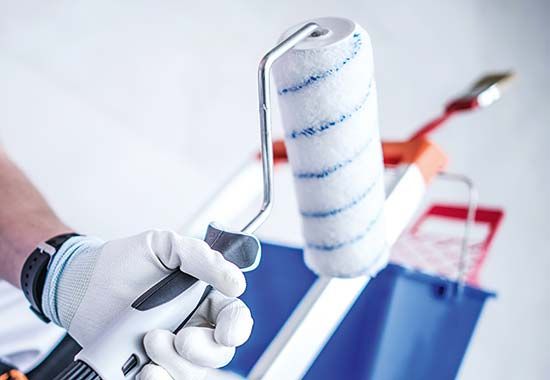 Eine Hand mit Arbeitshandschuh hält einen Farbroller über einer Farbschale.