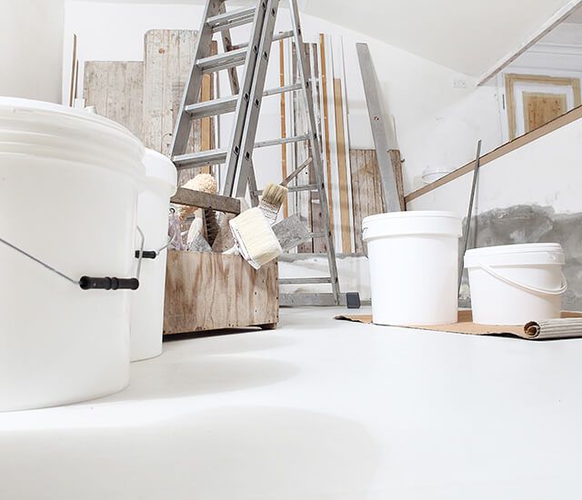 In einem renovierten Raum stehen Farbeimer, eine Leiter und Malerwerkzeug.