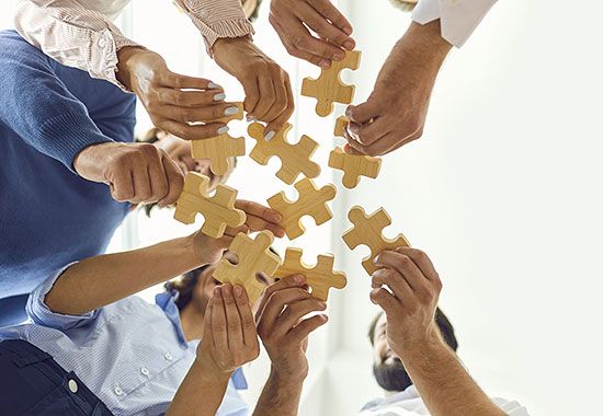 Mehrere Hände halten Holz-Puzzleteile und setzen sie zusammen.